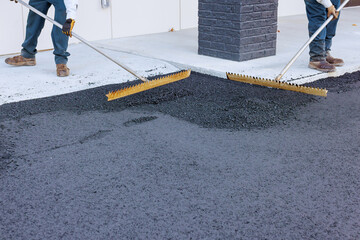Workers are leveling new asphalt on parking lot with large brooms in commercial area. © ungvar