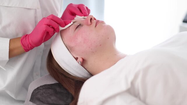 The beautician uses a hot pink glove to apply skincare treatment on the client, bringing a pop of color and uniqueness to the scene.