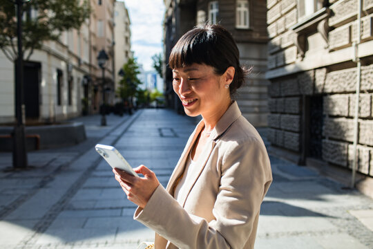 Smiling businesswoman using smartphone on a city street