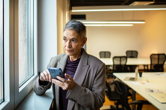Senior businesswoman using smartphone by window in modern office