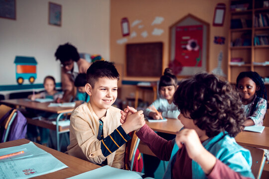 Two elementary schoolboys clasping hands in classroom