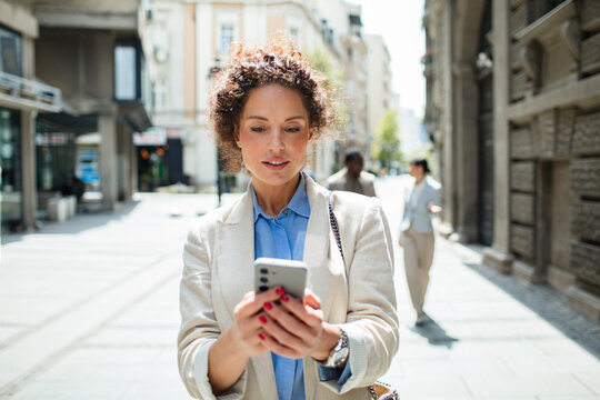 Businesswoman using smartphone on sunny city street