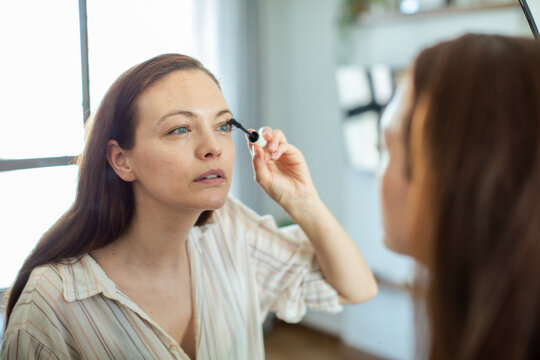 Woman applying mascara in mirror at home