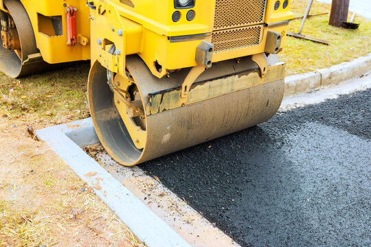 Heavy road roller compacts fresh asphalt on street being constructed in quiet suburban neighborhood