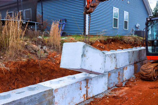 Workers use excavator machinery to position concrete blocks for retaining wall at home site