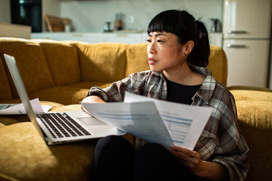 Woman reviewing household bills on laptop on living room sofa