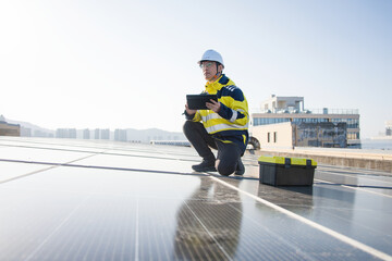 Fototapeta premium Engineer inspecting solar panels on rooftop while holding a tablet device