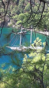 A majestic gulet floats serenely on the vibrant turquoise Aegean Sea, nestled in a secret Fethiye cove near Oludeniz. Verdant pines cling to Babadag Mountain's slopes, bathed in sunny Turkish splendor