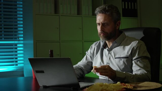 Freelancer working late with snacks. Businessman night routine with laptop. Business man at desk eating popcorn in late hours. Man rest at late office.