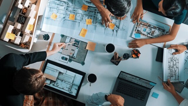 Top aerial view business people brainstorming about building interior at table with house model and laptop displayed house plan while architect engineer drawing and writing at blueprint. Alimentation.
