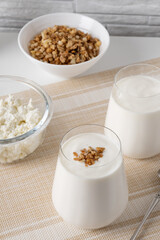 Kefir, buttermilk or yogurt, cottage cheese with granola. Yogurt in glass on white wooden background. Probiotic cold fermented dairy drink. Gut health, fermented products, healthy gut flora concept