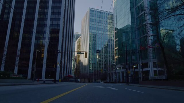 Modern glass skyscrapers line a city street during the day with clear skies