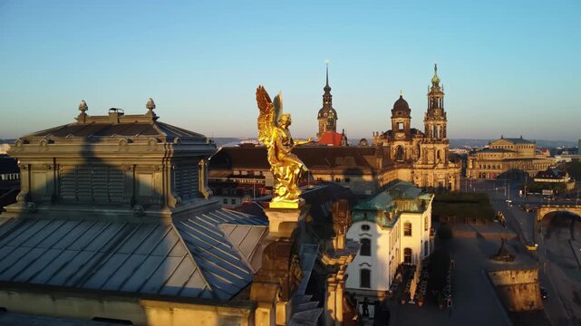 A pulling back aerial shoot of the statue of god Phantasos on the western corner risalit of the Dresden Art Academy  in the Lipsiusbau building under sunshine at dawn with the Frauenkirche, Dresden's 