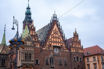 Obraz premium Wroclaw's Old Town Hall on the Rynek shows gables, clock, and spires, with a wrought iron lamp with golden spheres in front, on an overcast day with soft light.