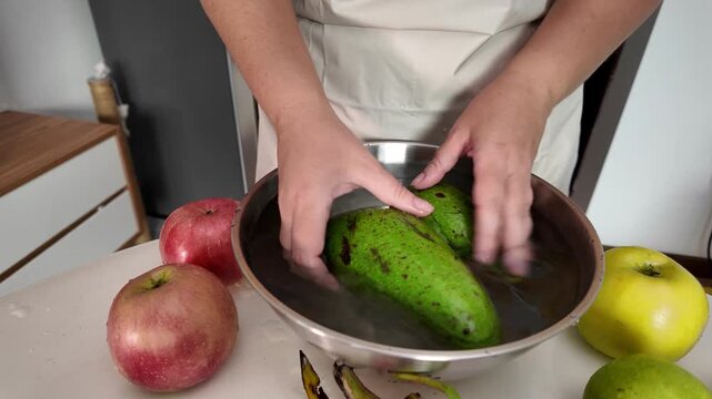 Hands of a woman , standing in front of a table with fruit and washing ripe avocados