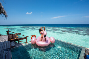 Woman sitting on a pink flamingo at the pool.Tropical island beach landscape exotic shore coast. Summer vacation, holiday amazing nature. Relax paradise, Maldives.