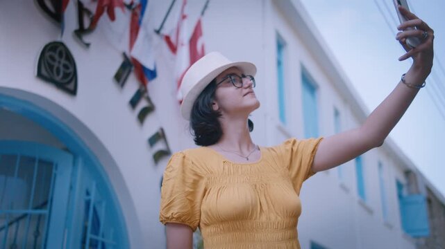 Elegant Woman in Hat Using Smartphone for Selfie on Charming European Alley with Traditional Architecture
