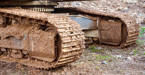 Heavy machinery crawler tracks covered in thick mud at a construction site. Close-up of industrial excavator treads in dirty terrain. © YuliiaKettu