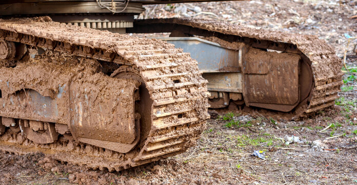 Heavy machinery crawler tracks covered in thick mud at a construction site. Close-up of industrial excavator treads in dirty terrain.