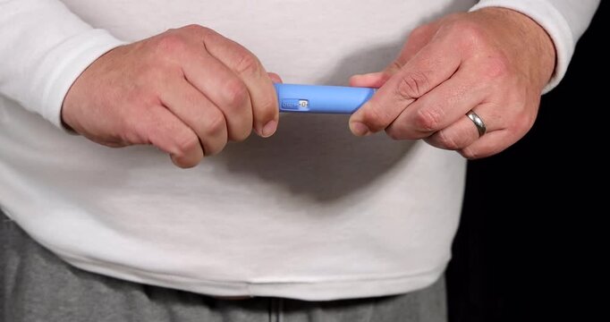 Close up of an obese person hands preparing a blue semaglutide GLP-1 injector pen for a subcutaneous weight loss treatment at home.