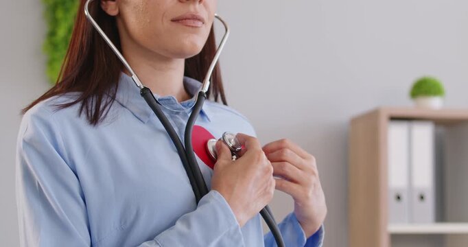 Woman using stethoscope for self heart health checkup. Person listening to heartbeat and pulse, holding red heart shape on chest, showing awareness of cardiovascular disease prevention and screening