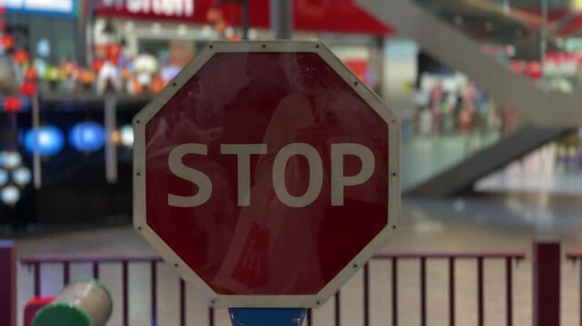 Red octagonal stop sign for children spinning inside an indoor playground, with the colorful, blurred background of a shopping mall creating a vibrant and playful atmosphere