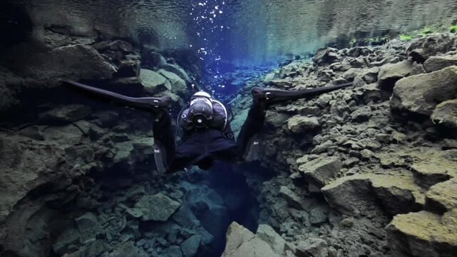 Person in a dry suit scuba diving in the crystal clear waters of a tectonic fissure