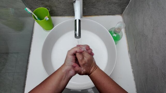 A woman washes her hands with soap over the sink in the bathroom. Personal hygiene