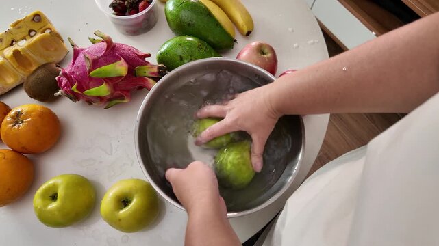 Hands of a woman , standing in front of a table with fruit and washing ripe pears in a metal bowl of water