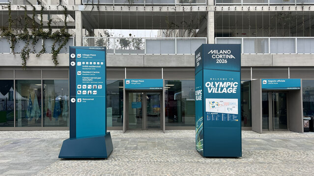 Milan, Italy - February 24, 2026: Milano Cortina 2026 Olympic Village entrance with teal wayfinding totems, Village Plaza sign and modern residential building facade.