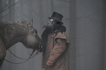 Mystisches Portrait eines dunklen Pferdes und einer mit Vogelmaske verkleideten Person in mystisch finstern Winterwald © Grubärin