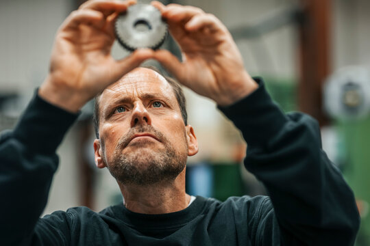 Focused mature male worker examining machine part while working in factory