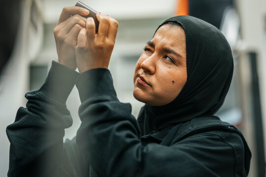 Female worker wearing hijab examining machine part while working in factory