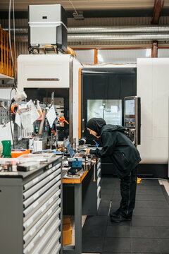 Full length of young female operative assembling machine parts while working in metal factory