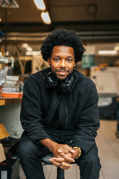 Portrait of male factory worker wearing ear protectors around neck while sitting with hands clasped