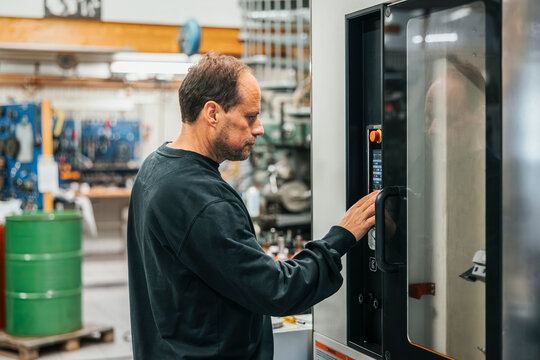 Mature male worker operating machine in factory plant