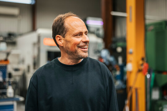 Smiling male manufacturing worker looking away while standing in factory