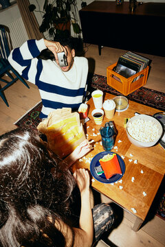 Young man photographing woman eating french fries at home