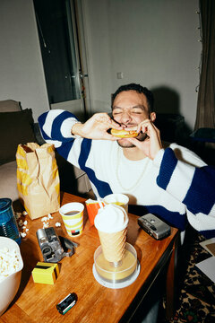 Young man eating burger with eyes closed at home