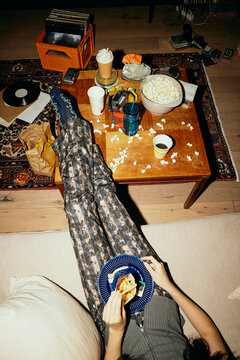 High angle low section view of young woman eating fast food with feet up on table at home