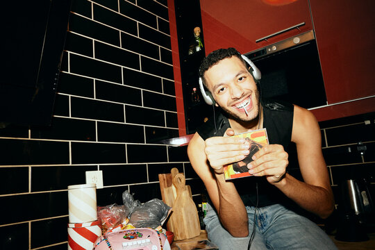 Portrait of happy man holding CD case and listening to music while sitting on counter in kitchen at home