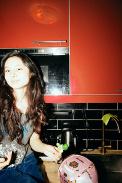 Smiling young woman holding candy while sitting on kitchen counter at home