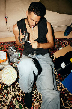 High angle view of young man using vintage video camera while sitting by sofa at home