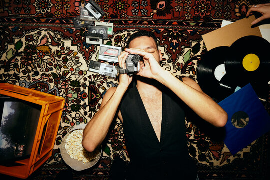 Directly above shot of young man filming through video camera while lying on carpet amidst music equipment at home