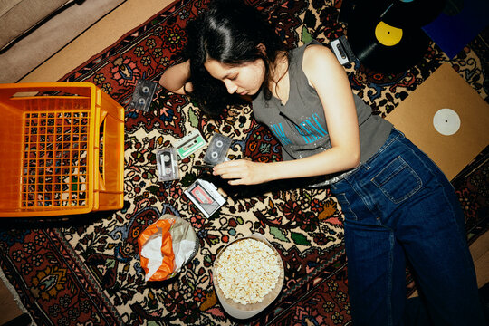 Directly above shot of woman checking audio cassettes while lying on patterned carpet at home