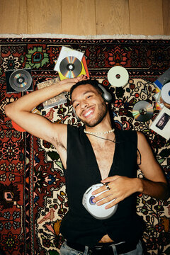 Portrait of happy man listening to music through personal stereo while lying on patterned carpet