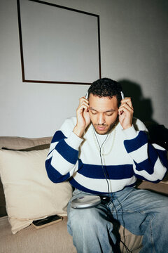 Young man listening to music through personal stereo while sitting on sofa at home
