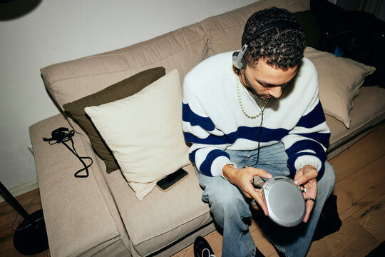 High angle view of young man operating personal stereo while sitting on sofa