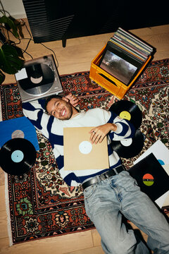 High angle view of smiling man lying down on carpet amidst record vinyls at home