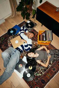 High angle view of young friends lying down on carpet with record vinyls at home